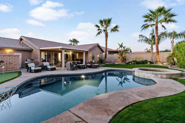 Backyard with kidney-shaped pool, attached spa, and wicker lounge seating under a covered patio, palm trees in the yard.